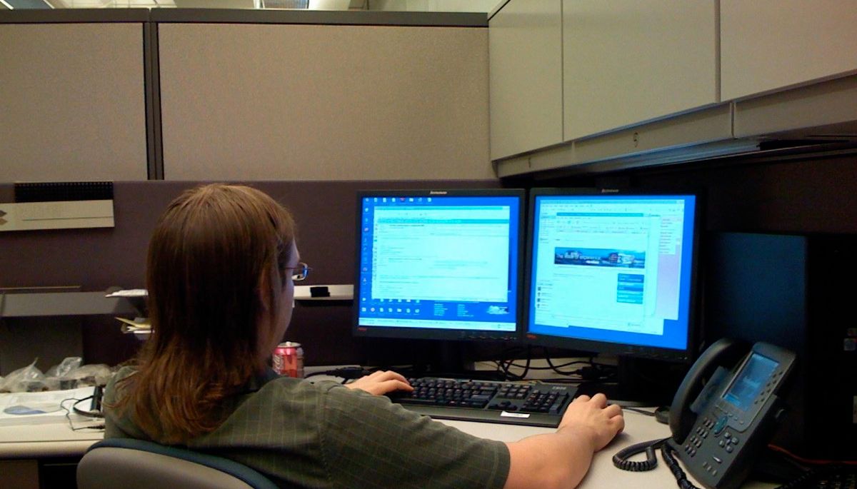 An office worker at a desk with dual computer monitors representing desktop productivity tasks